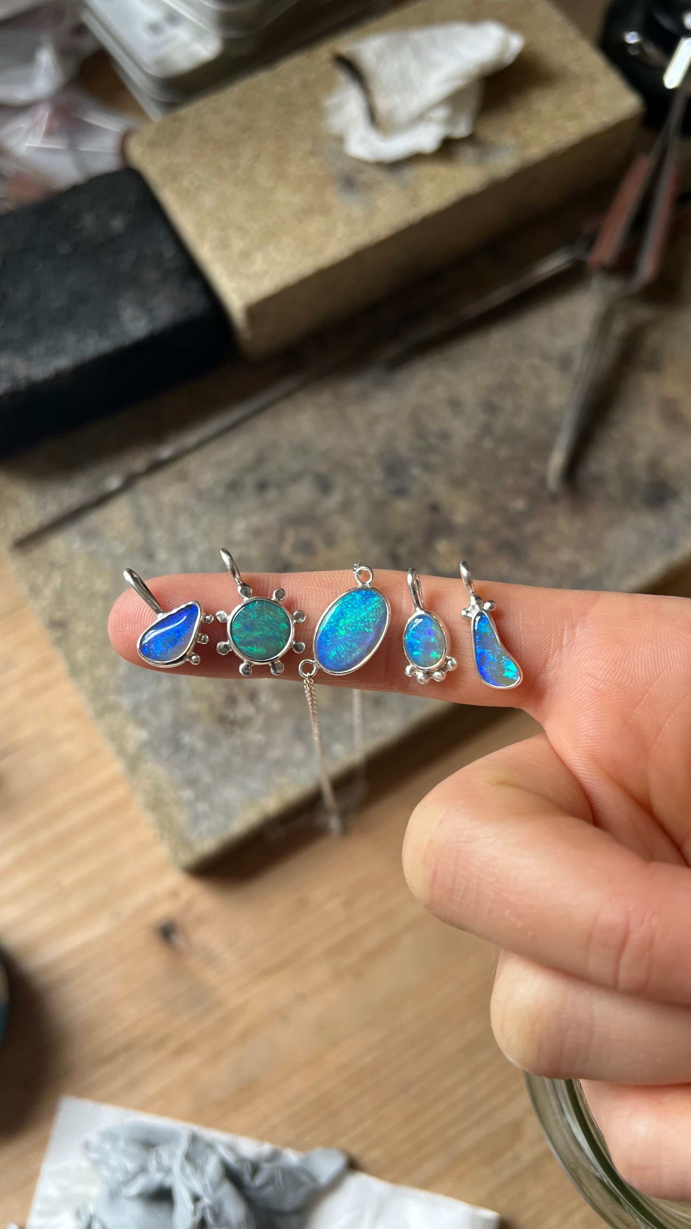 Fünf Opalanhänger mit blauen und grünen Steinen auf einem Finger